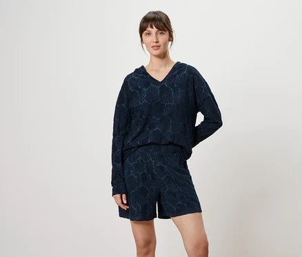 Une femme porte un haut à manches longues bleu marine à motifs avec un col en V et un short devant un fond neutre.