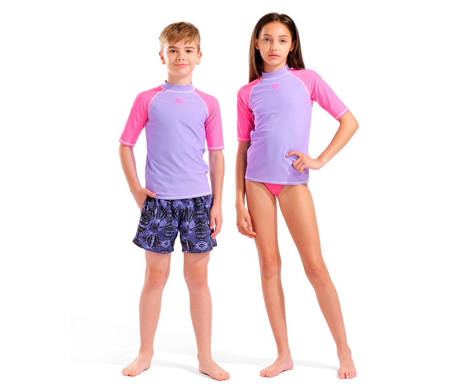 Un garçon portant un haut de bain à manches courtes lilas et rose et un short de bain à motifs se tient à côté d'une fille portant un haut de bain à manches courtes lilas et rose et un slip de bain rose.