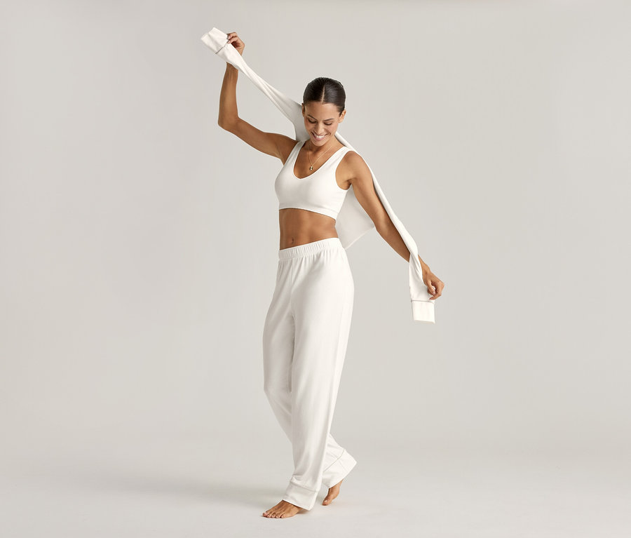 Femme en ensemble pyjama et brassière sans coutures, crème, tenant le haut.