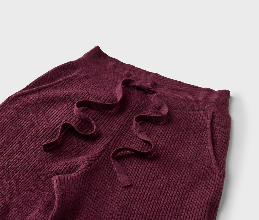 Gros plan d'un pantalon côtelé bordeaux avec cordon de serrage et poche latérale.