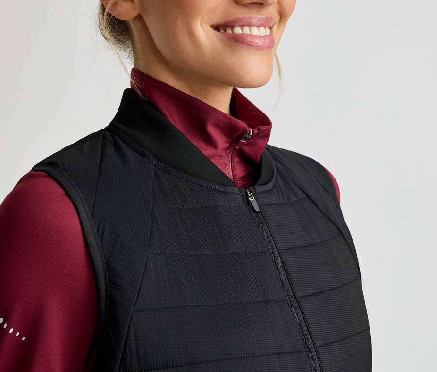 Femme portant un haut rouge à manches longues et une veste sans manches noire matelassée zippée.