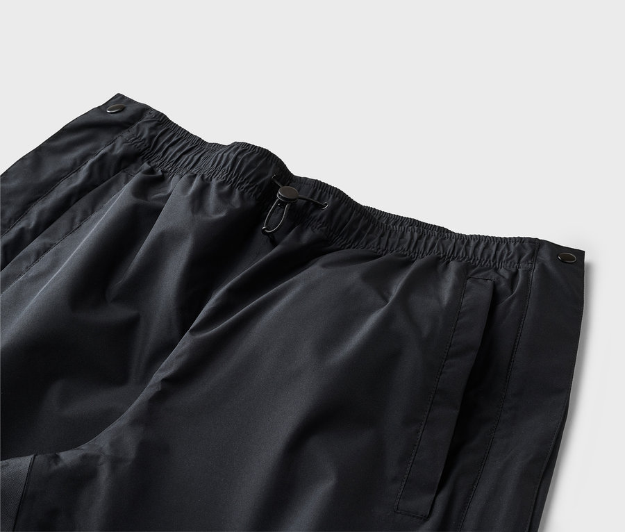 Gros plan d'un pantalon noir avec taille élastique, cordon de serrage et poche latérale sur fond neutre.
