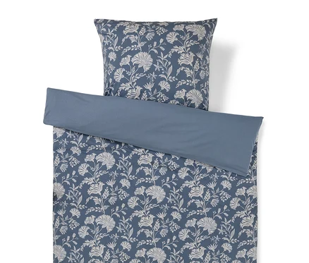 Une housse de couette bleue et une taie d'oreiller assortie avec un motif floral blanc, avec une section unie bleue repliée sur le dessus.
