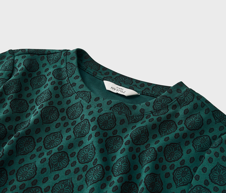Gros plan d'un haut vert émeraude avec un motif noir et une étiquette blanche indiquant « TCHIBO MY STYLE ».