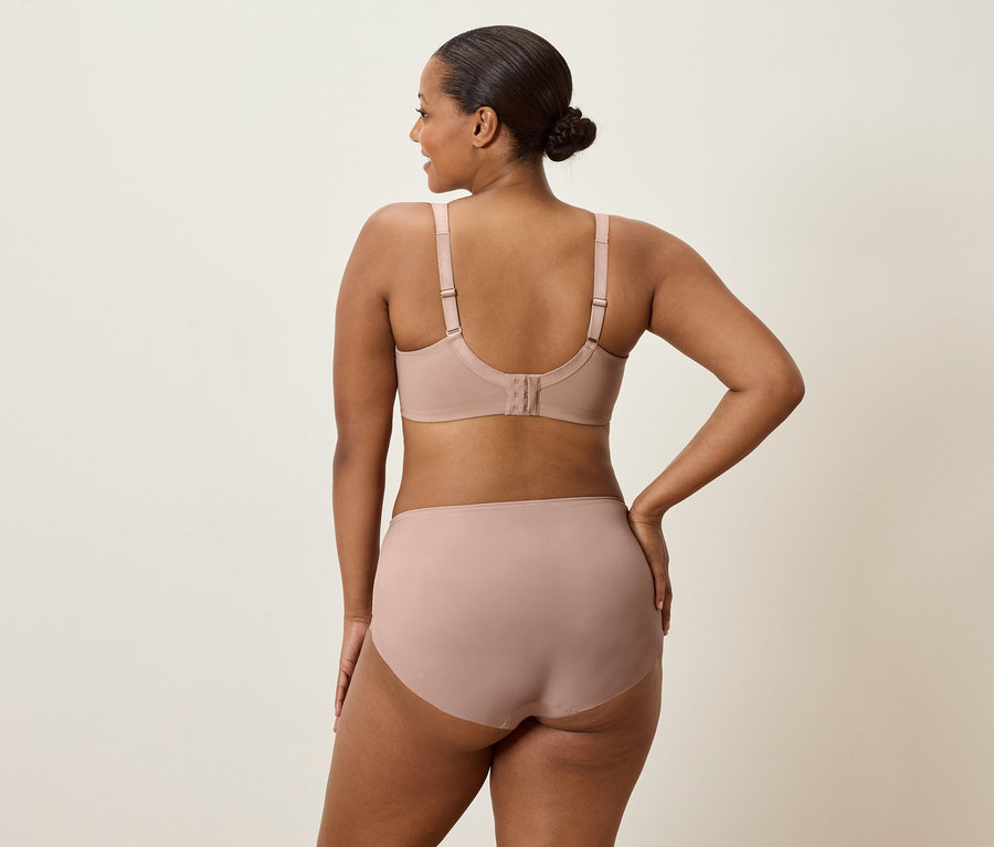 Une femme vue de dos portant un soutien-gorge et une culotte couleur chair, avec une main sur la hanche.