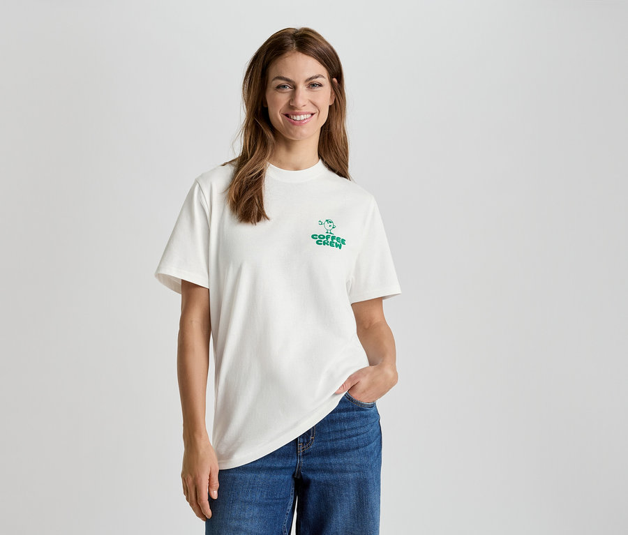 Femme portant un t-shirt blanc avec l'inscription "Coffee Crew" et un jean bleu.