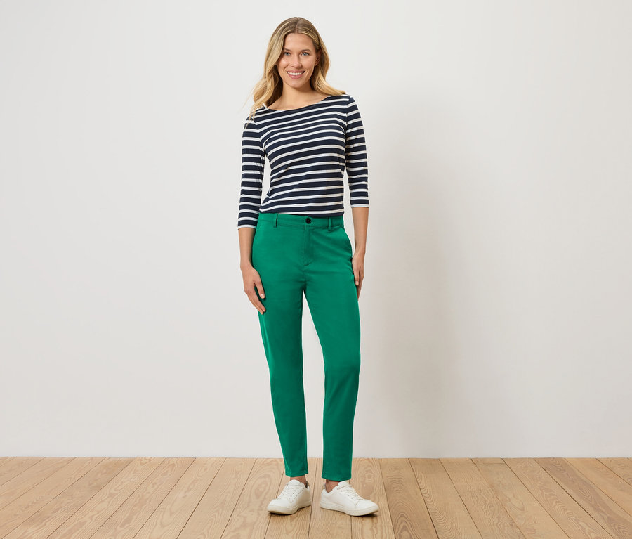 Une femme porte un haut rayé bleu et blanc, un pantalon vert et des baskets blanches.