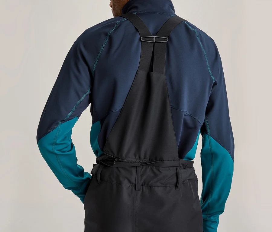 Dos d'une personne portant un haut à manches longues bleu foncé et sarcelle et une salopette noire à bretelles. Une fermeture éclair est visible à l'arrière du pantalon.