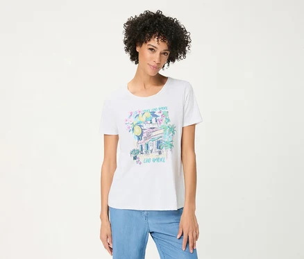 Femme aux cheveux bouclés portant un T-shirt Olsen blanc avec un imprimé placé coloré de citrons, fleurs, un bâtiment, des palmiers et le texte "CIAO AMORE", et un jean bleu clair.