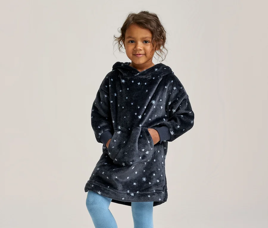 Une jeune fille sourit, vêtue d'un sweat à capuche oversize bleu foncé à étoiles blanches et d'un legging bleu clair, les mains dans la poche avant.