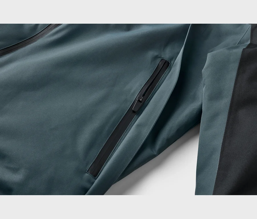 Gros plan d'une veste sarcelle avec une poche zippée noire et un panneau latéral noir.