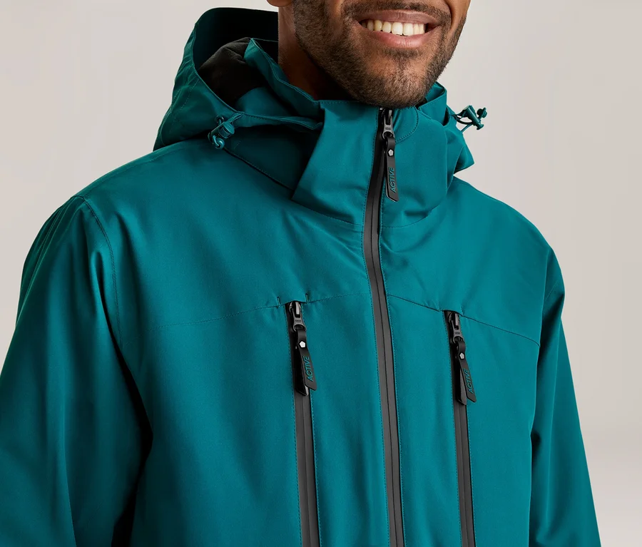 Homme souriant portant une veste à capuche turquoise avec une fermeture éclair principale et deux fermetures éclair sur la poitrine.