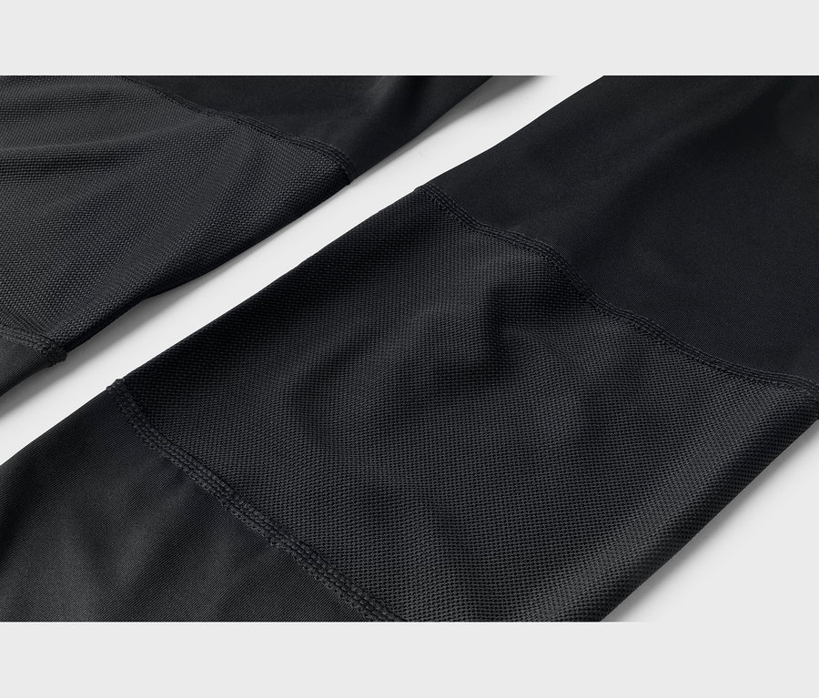 Gros plan sur un tissu noir avec des sections lisses et texturées en grille, reliées par des coutures.