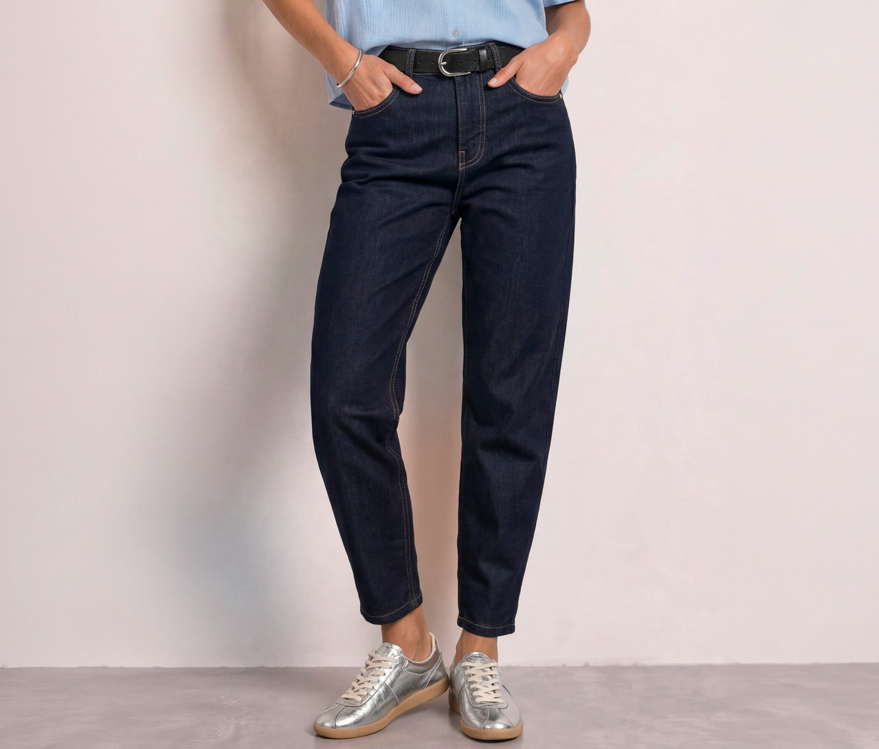 Personne portant un jean barrel Street One bleu foncé, un haut bleu clair, une ceinture noire et des baskets argentées, les mains dans les poches.