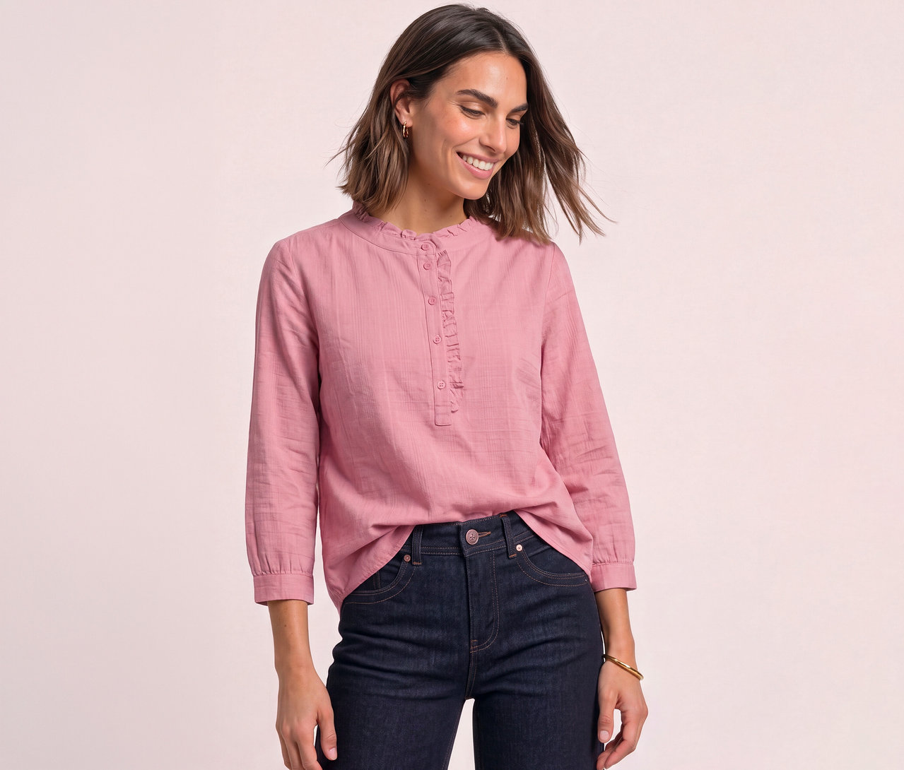 Une femme souriante porte un chemisier en velours côtelé Street One rose pâle à volants et un jean foncé.