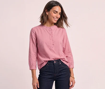 Une femme souriante porte un chemisier en velours côtelé Street One rose pâle à volants et un jean foncé.