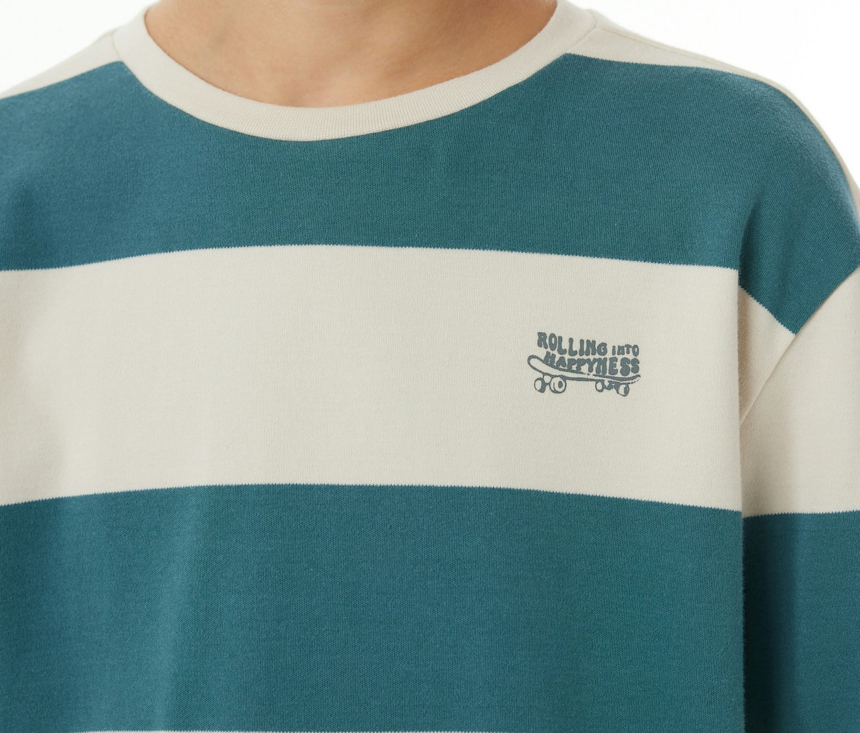 Gros plan d'une personne portant un haut de pyjama SCHIESSER Kinder-Interlock rayé. Il présente des rayures crème et sarcelle, et une broderie skateboard avec 'ROLLING INTO HAPPINESS'.