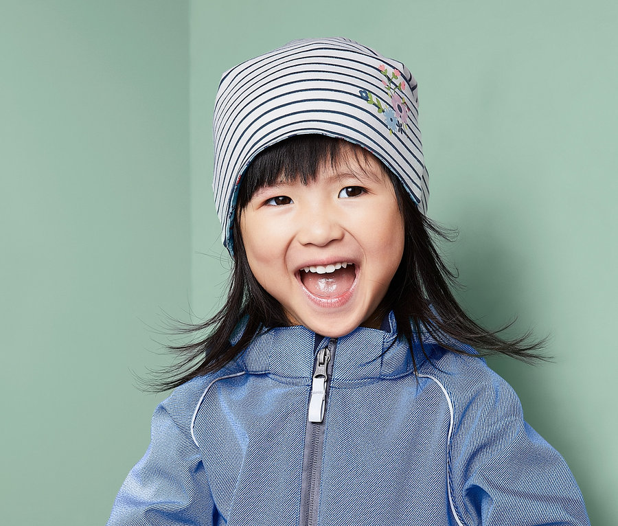 Fillette souriante portant une combinaison bleue et un bonnet réversible.