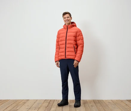 Un homme debout portant une doudoune orange, un pantalon bleu marine et des chaussures noires.