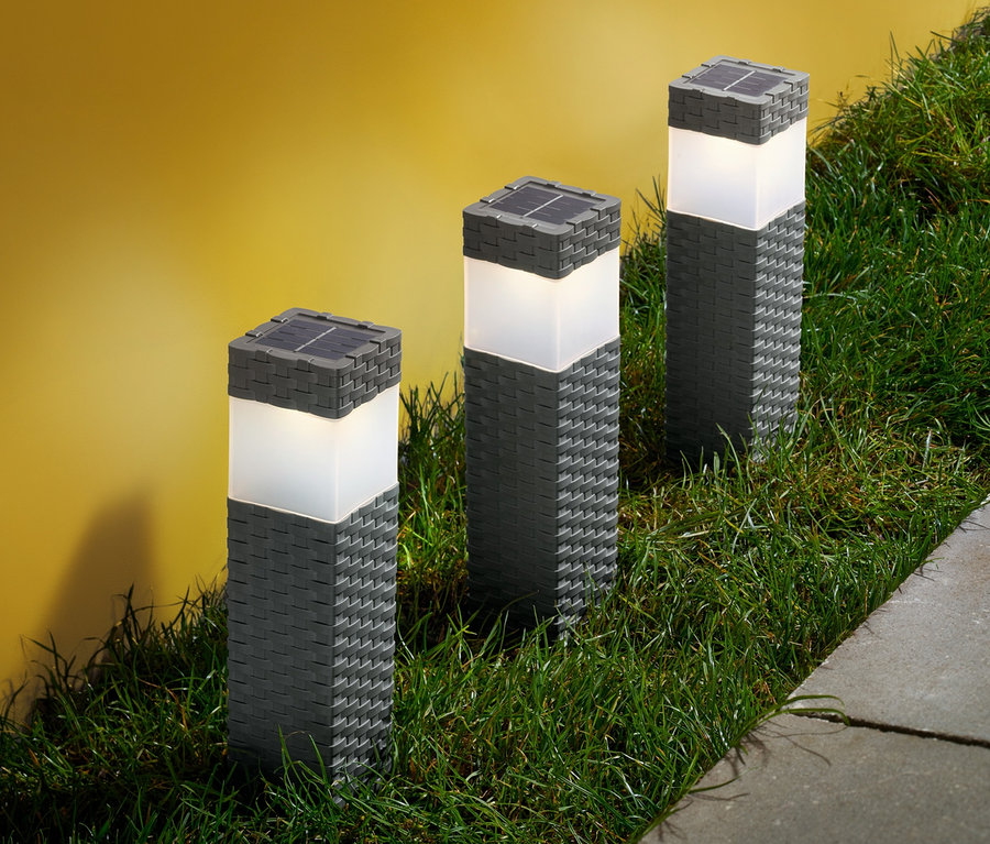 Trois colonnes solaires sont posées dans l'herbe à côté d'une allée.
