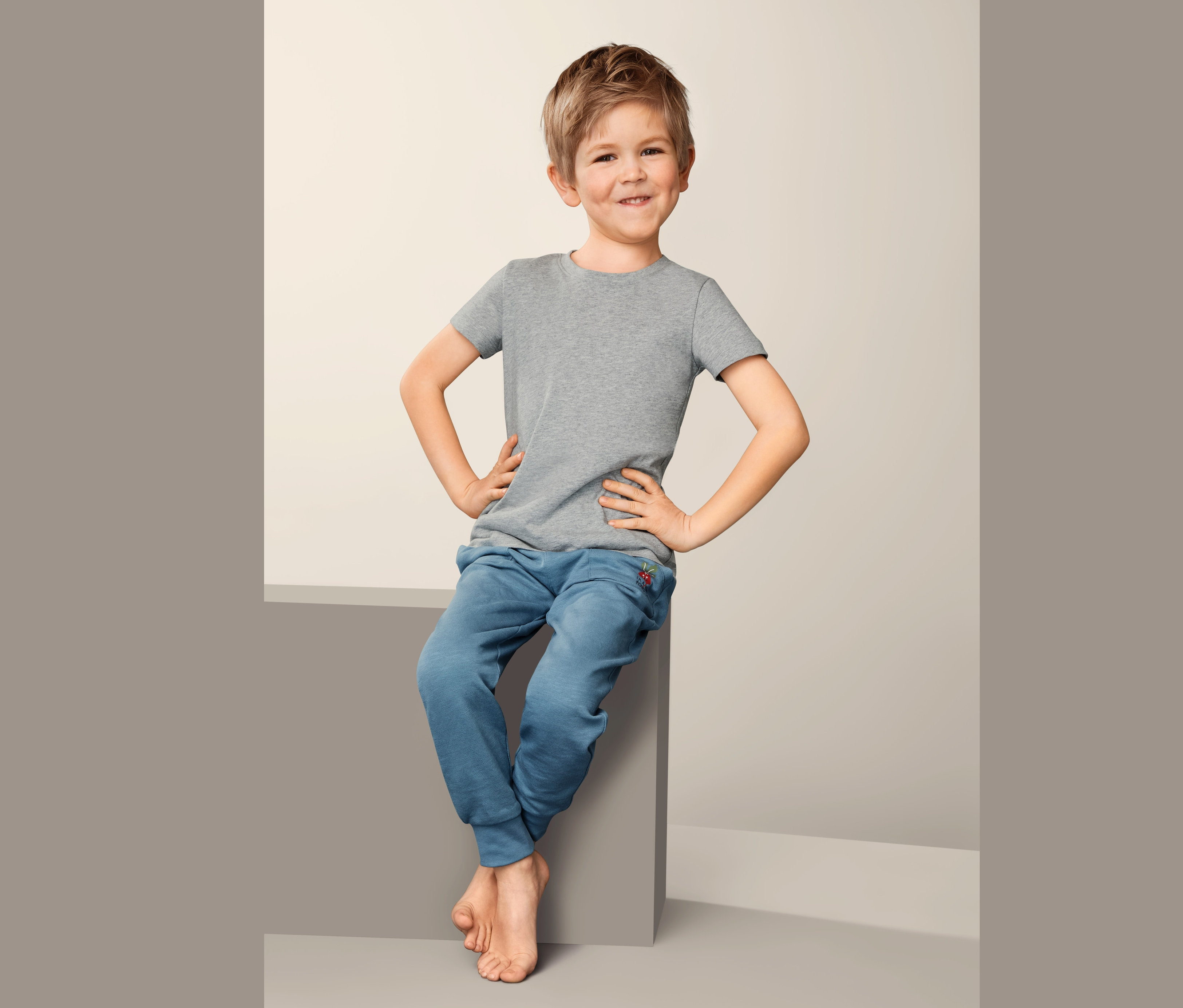 Un garçon est assis et porte 2 maillots de corps et un pantalon de survêtement bleu.