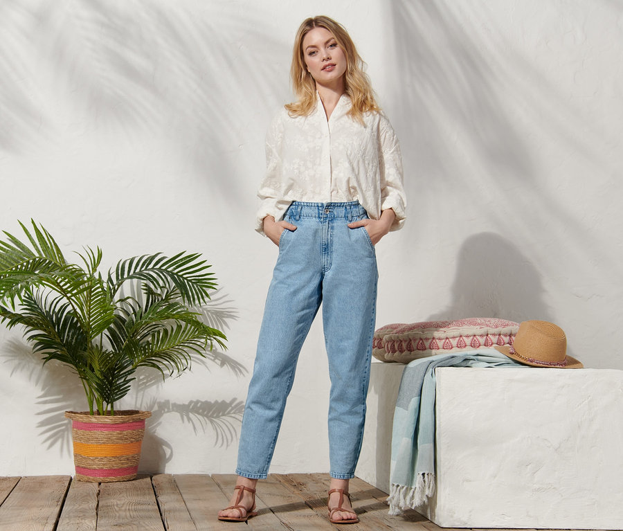 Une femme blonde pose en jean décontracté, chemisier et sandales.