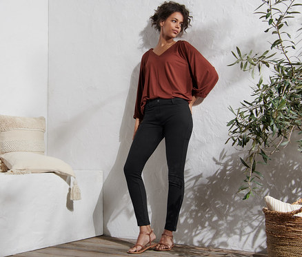 Femme posant en jegging noir, chemisier marron et sandales.