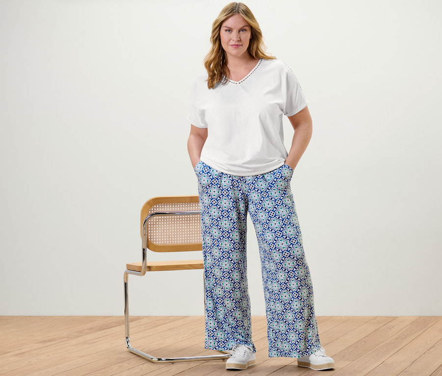 Une femme pose dans une blouse blanche avec ruban au crochet et un pantalon palazzo à imprimé intégral.