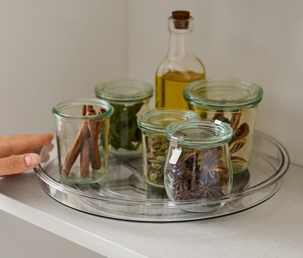 Une main atteignant un plateau tournant avec des épices sur une étagère.