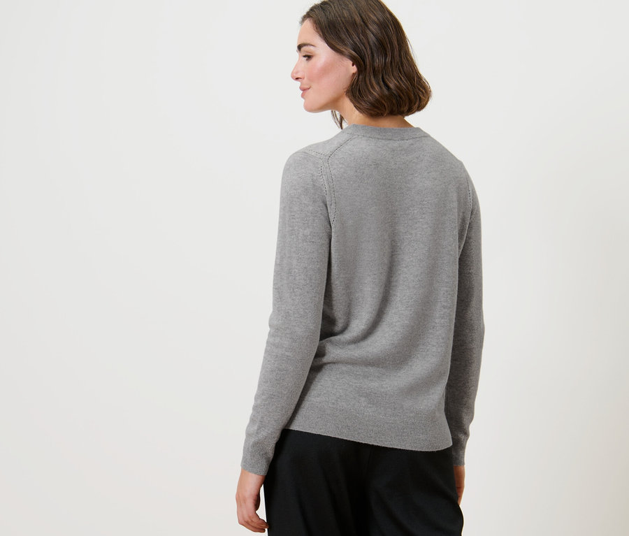 Une femme regardant par-dessus son épaule porte un pull en maille fine avec du cachemire gris chiné.