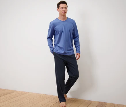 Un homme debout portant un pyjama bleu/bleu foncé.