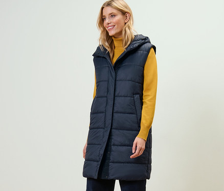 Une femme porte un long gilet sans manches matelassé avec capuche.