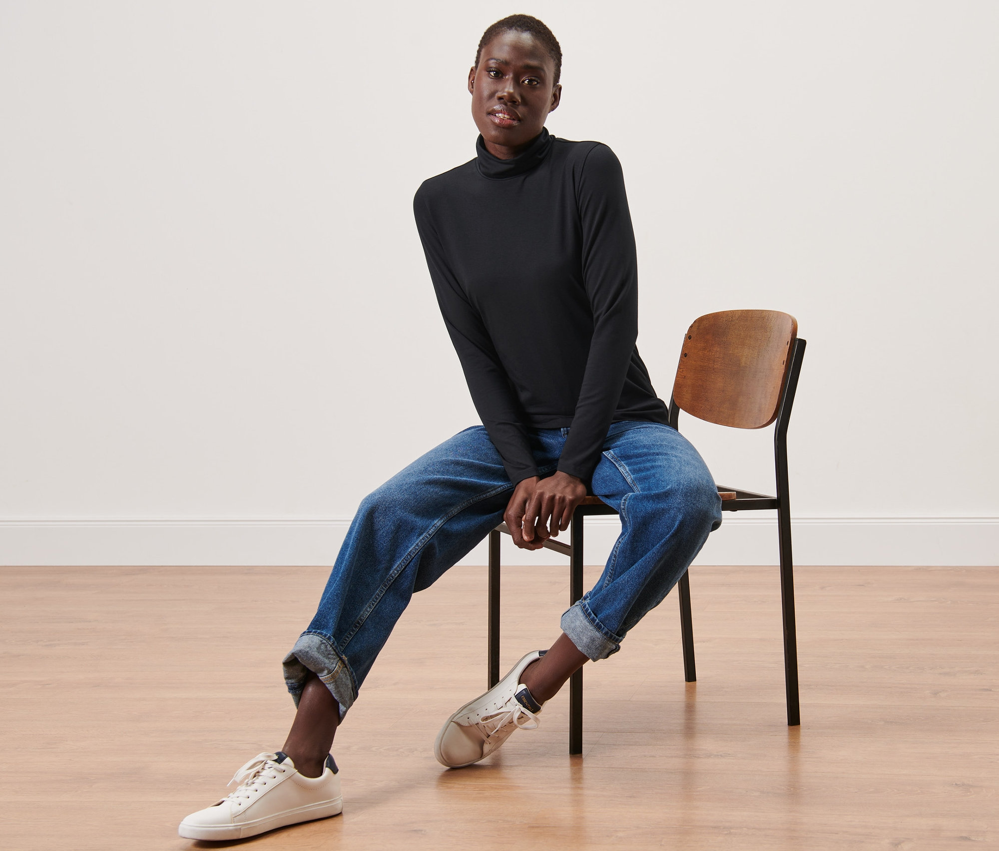 Une femme assise sur une chaise portant un t-shirt noir à col roulé.
