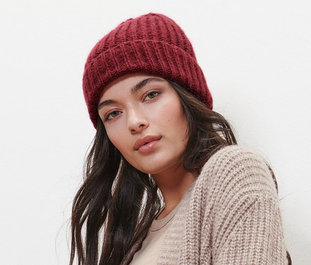 Femme posant avec un bonnet en maille avec de la laine, un cardigan beige et un jean.