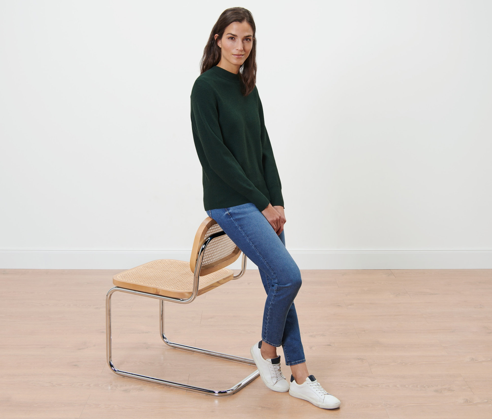 Femme assise sur une chaise portant un pull en maille fine, un jean et des baskets.