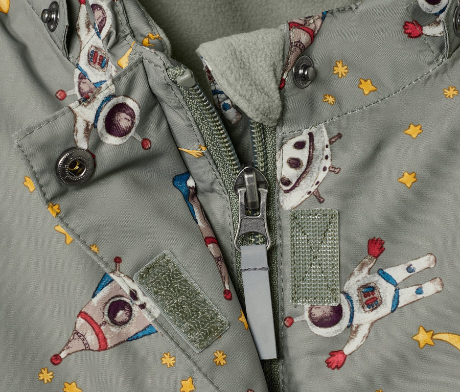 Gros plan sur un vêtement de neige pour enfant avec un motif spatial et une fermeture éclair ouverte.