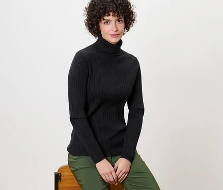 Une femme est assise sur une chaise et porte un pull à col roulé côtelé noir.