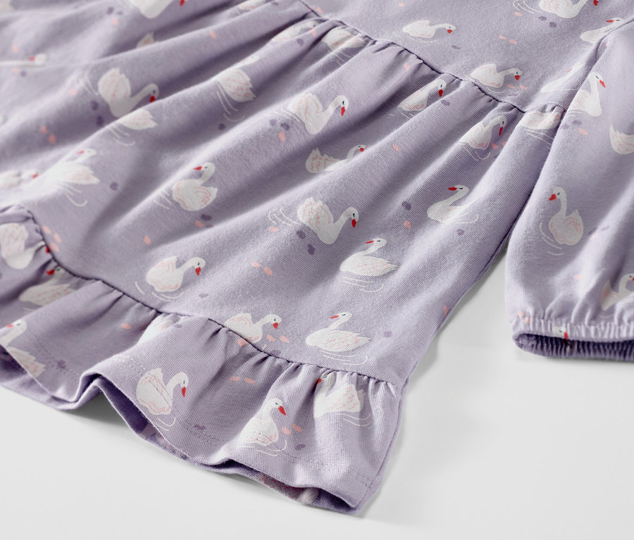Gros plan sur une robe en jersey lilas pour bébé avec un motif de cygnes.
