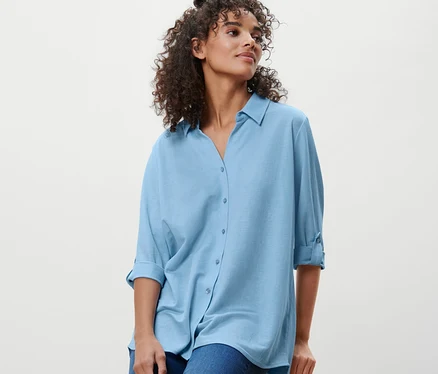 Une femme est assise sur un tabouret et porte un chemisier en jersey piqué bleu clair et un jean.