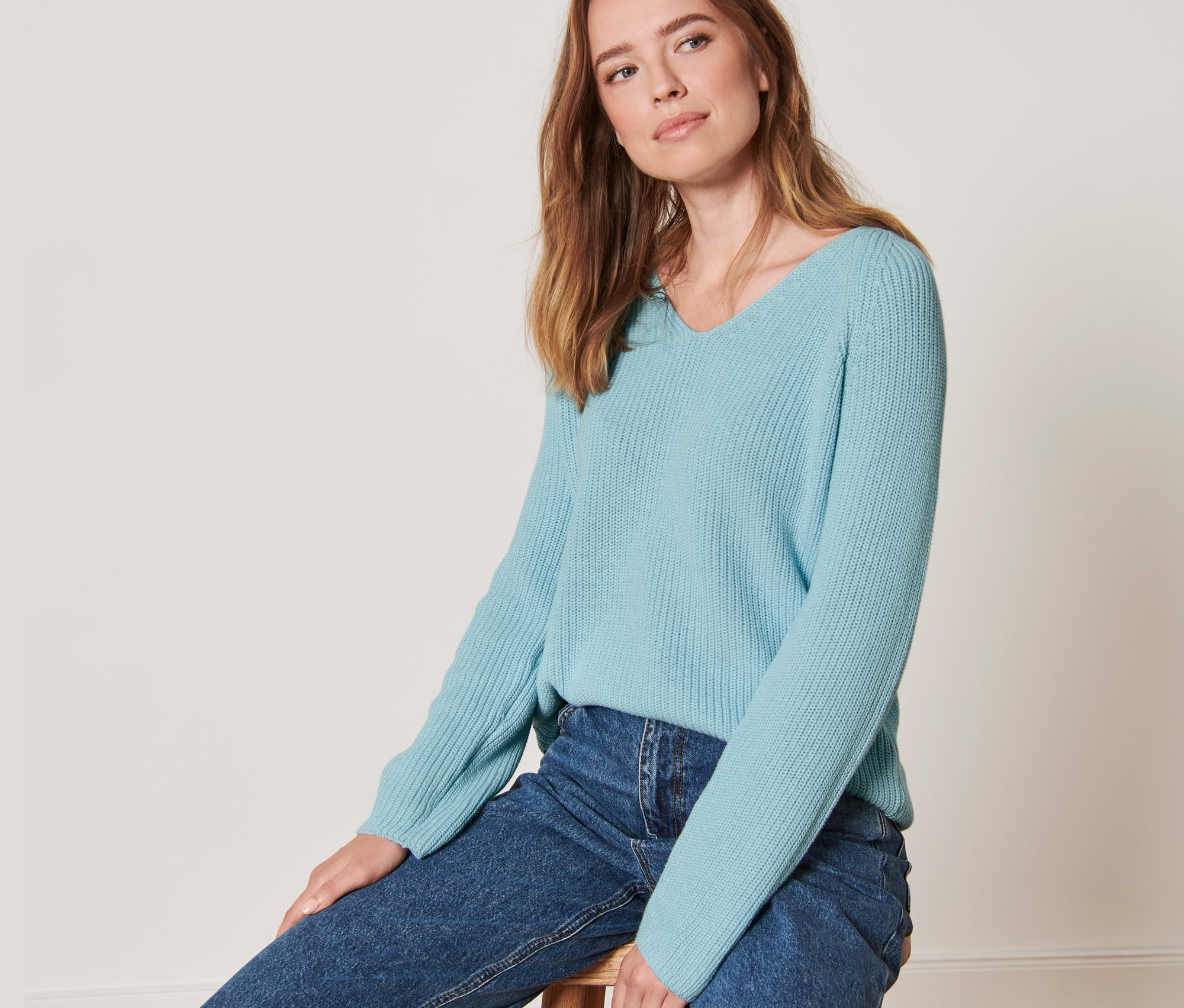 Une femme est assise sur un tabouret et porte un pull en maille bleu ciel.