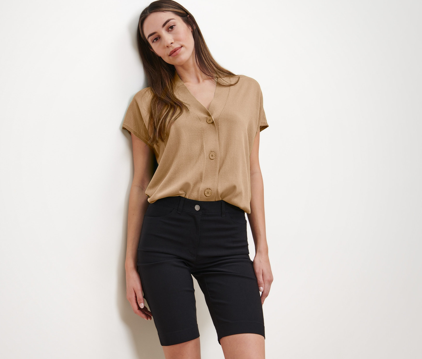 Une femme pose en chemisier beige et bermuda en bengaline noir.