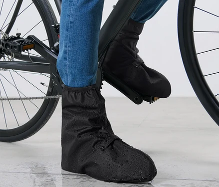 Pieds d'un cycliste en jean bleu et couvre-chaussures de pluie noirs sur un vélo.