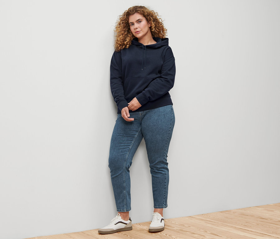 Une femme debout contre un mur porte un sweat-shirt à capuche bleu foncé.