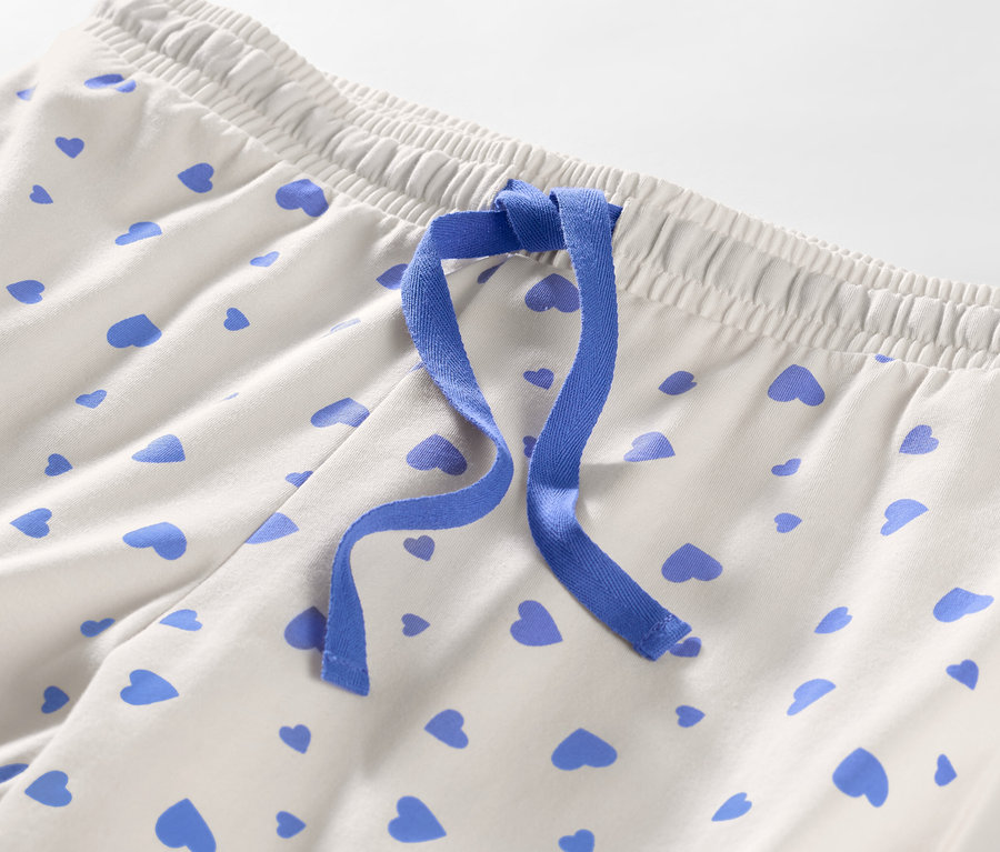 Détail d'un pantalon de pyjama à cœurs avec un ruban bleu.