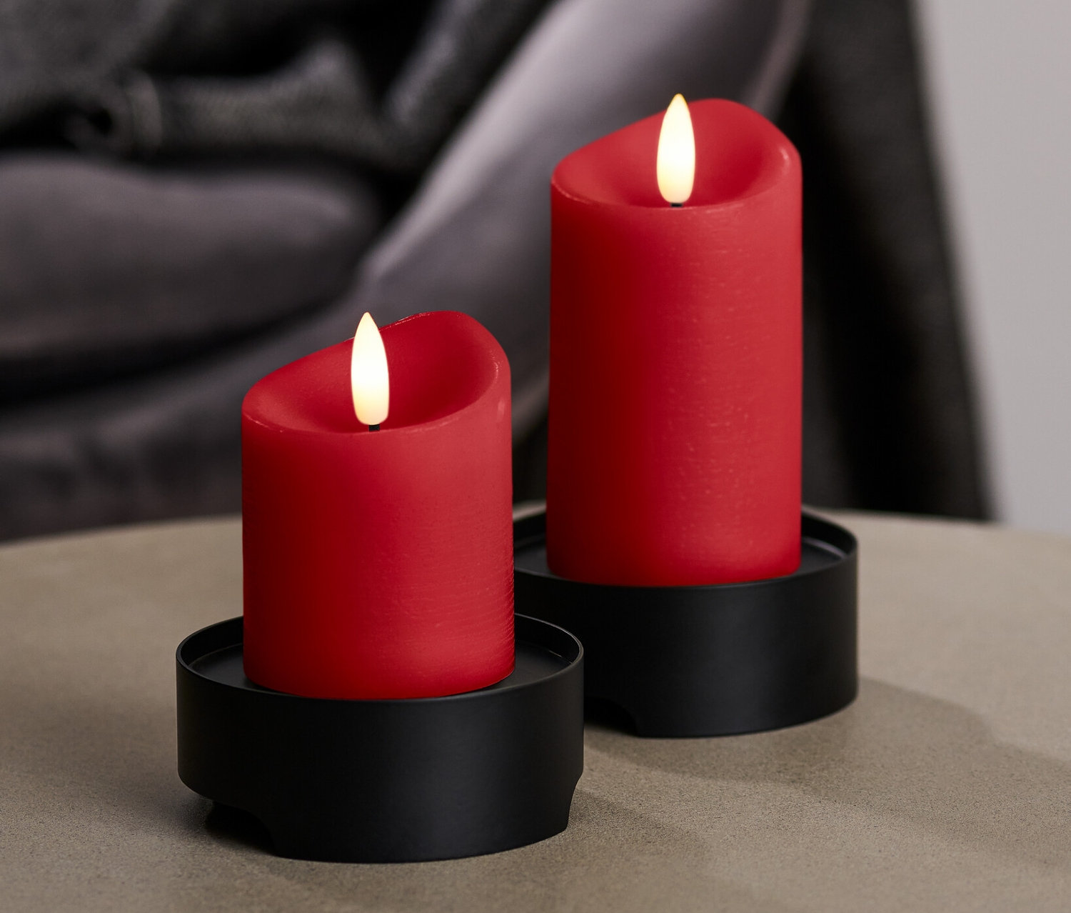 Deux bougies à LED en cire véritable rouges sur des supports noirs sont posées sur une table.
