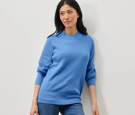 Femme posant en pull bleu en maille fine et jean.