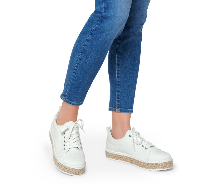 Jambes d'une femme portant un jean et des baskets en toile blanches.