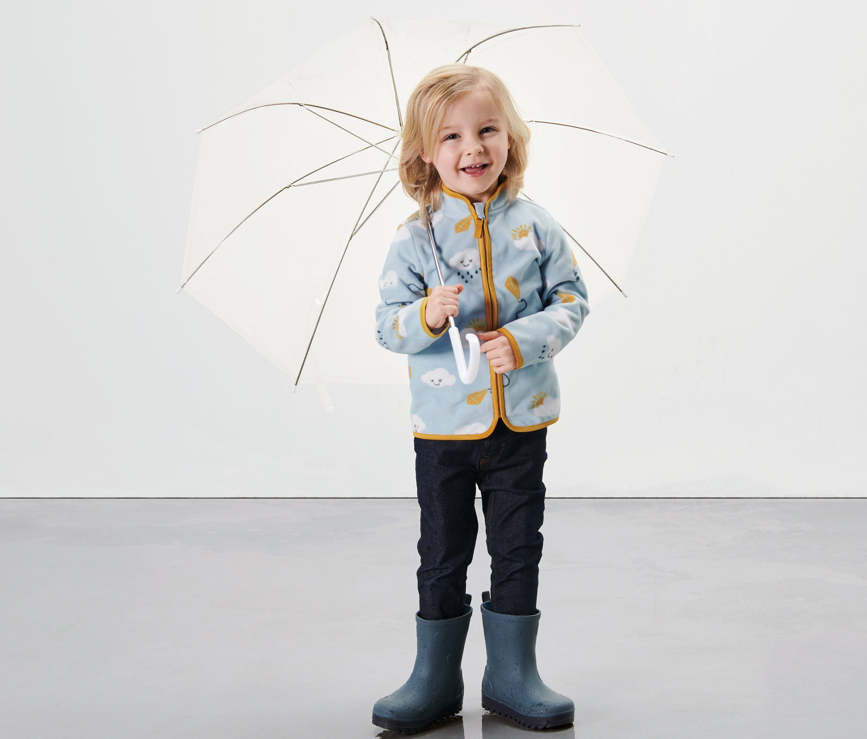 Un enfant tient un parapluie ouvert et porte une veste en polaire pour tout-petit, imprimé intégral.
