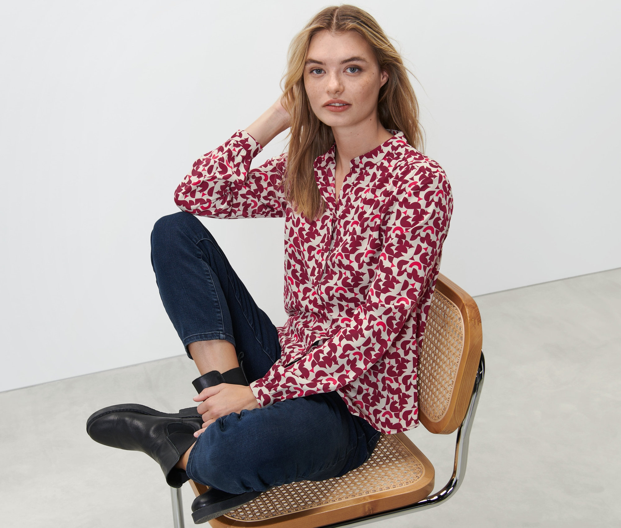 Femme assise sur une chaise portant un chemisier imprimé.