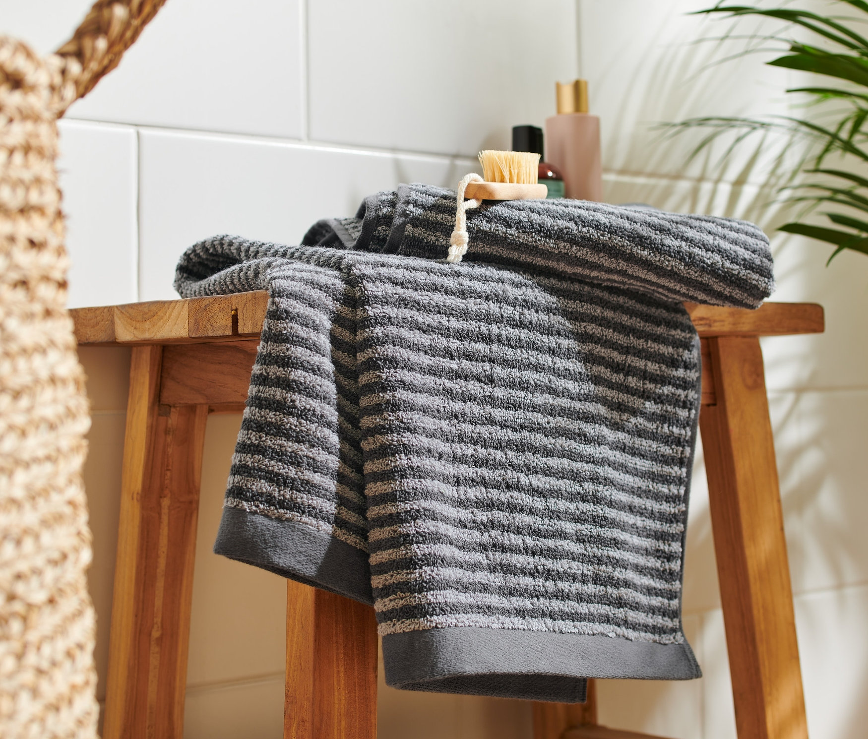 Deux linges de toilette anthracite de haute qualité sont posés sur un tabouret en bois.